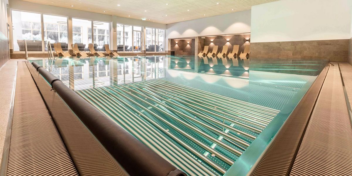 Innenansicht eines Schwimmbads mit Liegestühlen und großen Fenstern