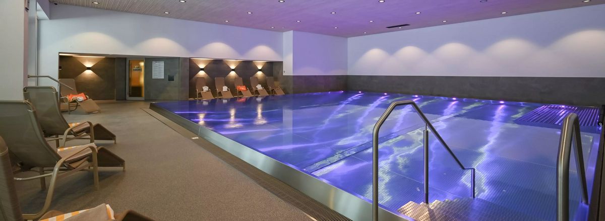 Innenpool mit blau beleuchtetem Wasser und Liegestühlen am Rand