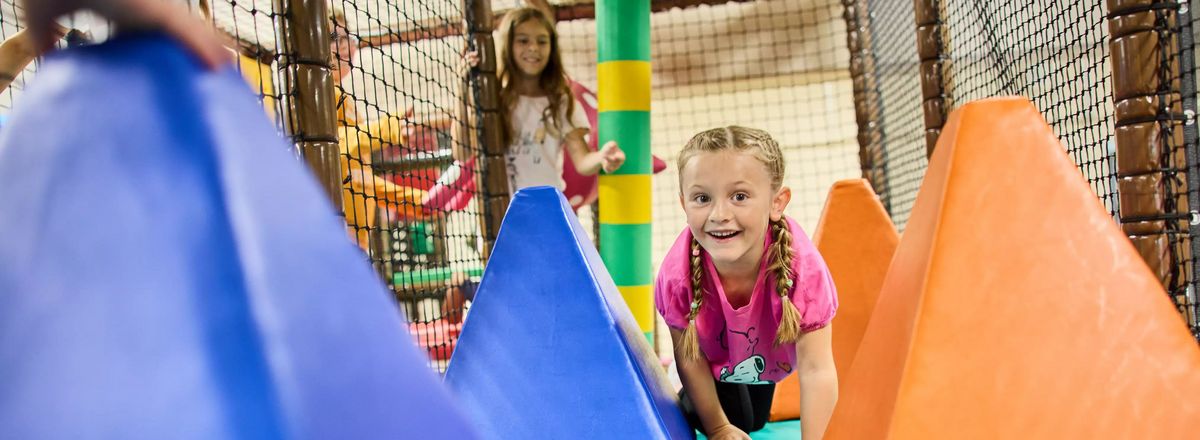 Mädchen krabbelt im Indoor-Spielbereich zwischen bunten Schaumstoff-Elementen
