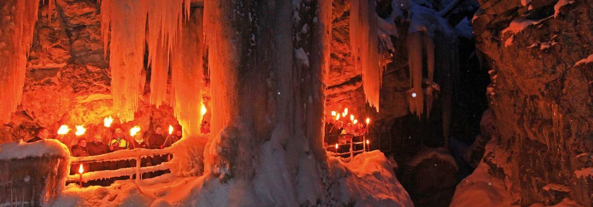 Beleuchtete Eishöhle mit Fackelwanderung im Winter