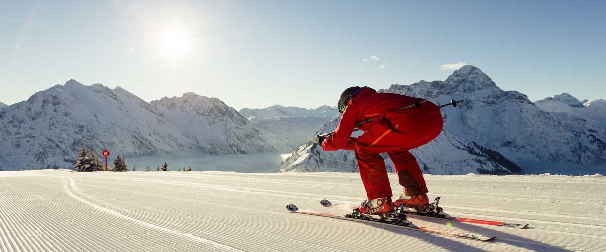 Skifahrer in roter Ausrüstung auf frisch präparierter Piste bei Sonnenschein