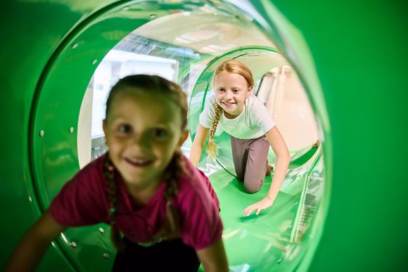 Zwei Mädchen spielen in einer grünen Röhre im Indoor-Spielplatz